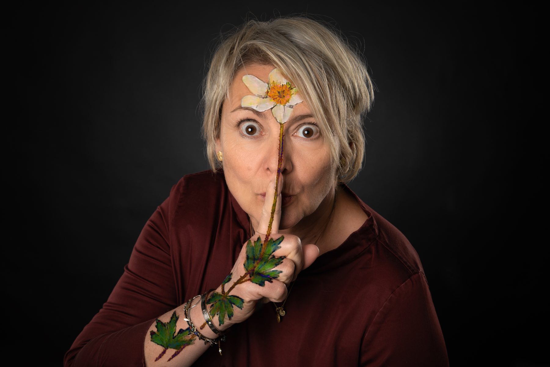 Portrait d’Anne Durrant-Cardis, une anémone peinte sur le front et la main, l’index posé sur les lèvres.